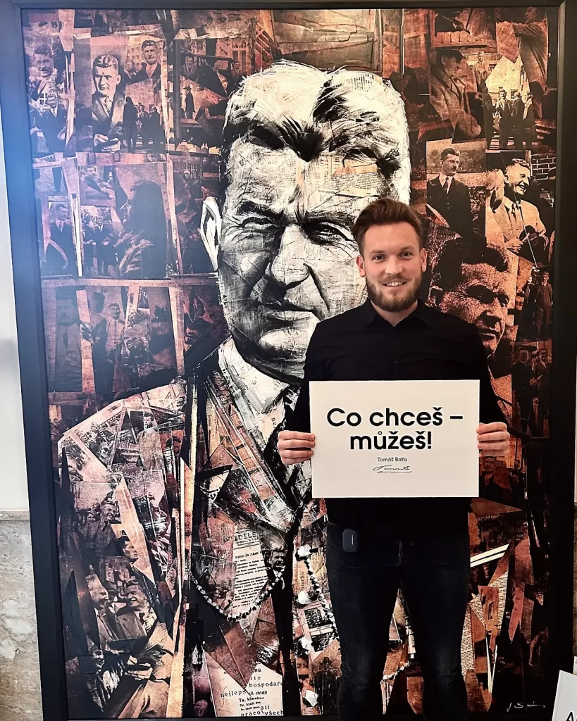 Jakub Kratochvíla před portrétem Tomáše Bati s cedulí „Co chceš – můžeš!“